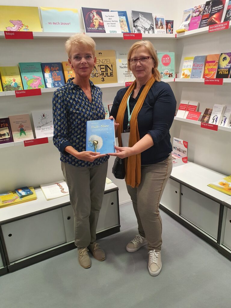 Foto von Maria Brand mit ihrer Verlegerin und dem Gedichtband Pusteblume auf der Buchmesse 2022
